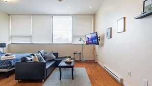 Een moderne woonkamer met een bank, een salontafel, een televisie en een raam met zonwering.