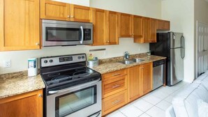 A kitchen with wooden cabinets, stainless steel appliances, granite countertops, and a white tiled floor. - Quaint Loft with AC, Abundance of Sunlight (Halifax)