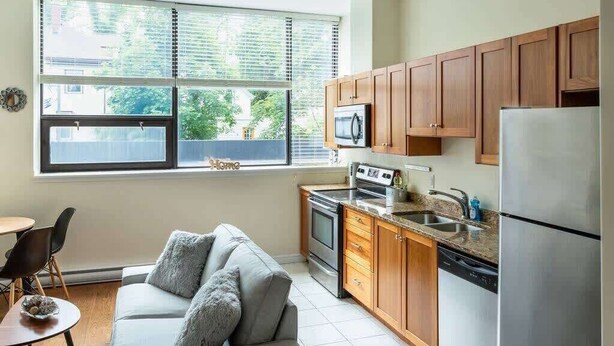 A compact kitchen with wooden cabinets, a stainless steel refrigerator, a microwave, and a dishwasher. - Quaint Loft with AC, Abundance of Sunlight (Halifax)