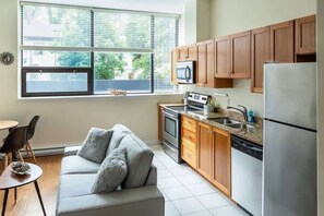 A compact kitchen with wooden cabinets, a stainless steel refrigerator, a microwave, and a dishwasher. - Quaint Loft with AC, Abundance of Sunlight (Halifax)