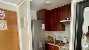 Une cuisine de taille réduite, dotée d’un réfrigérateur en acier inoxydable, de meubles de rangement en bois, d’un évier et d’une cuisinière.