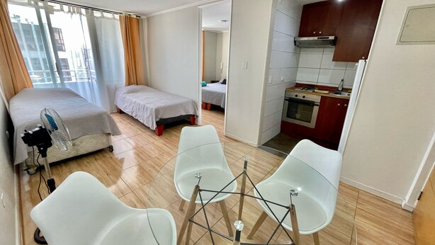 Une chambre d’hôtel de taille réduite comprenant un lit, une petite kitchenette et un coin salon avec des chaises.