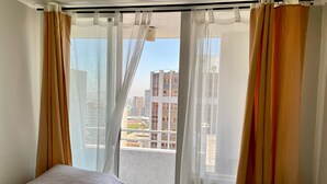 Une chambre d’hôtel avec deux lits, des rideaux légers et une vue sur le paysage urbain.
