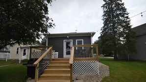 A wooden deck with a railing leading to a house with a gray exterior and a white door. - 3BR Newly Renovated House in the heart of Sturgeon Bay (Sturgeon Bay)