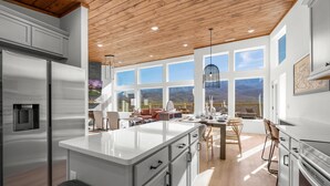 Una cocina moderna con una isla grande, electrodomésticos de acero inoxidable y vistas a montañas a través de amplios ventanales.