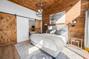 Une chambre avec un grand lit, des murs en bois, un luminaire suspendu et un tableau accroché au mur.