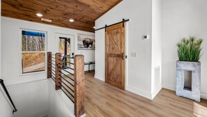 Una escalera de madera con barandilla de metal, una puerta de estilo granero y una planta en maceta.