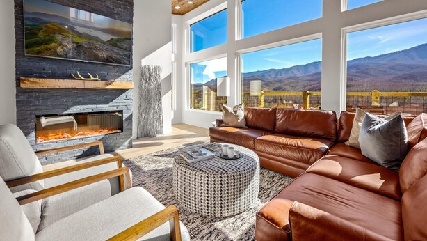Un salón moderno con chimenea de piedra, sofá de cuero y amplios ventanales con vistas a la montaña.