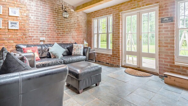 Ein gemütliches Wohnzimmer mit Ledersofa, einer Holzbank und einem großen Fenster mit Blick auf den Garten.
