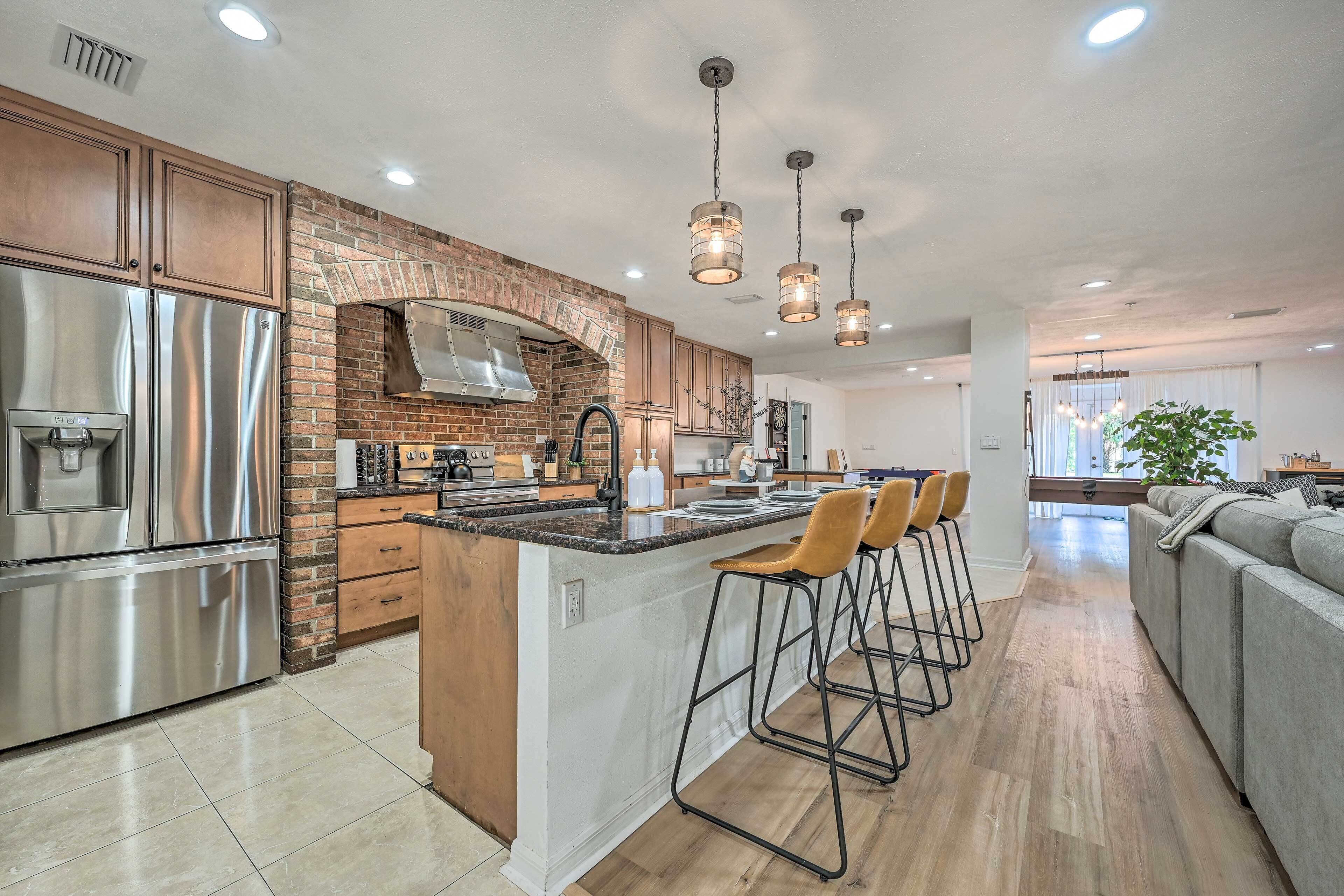 A modern kitchen with a central island, stainless steel appliances, and a brick backsplash.