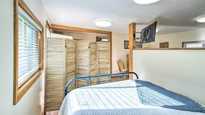 A bedroom with a bed, a TV mounted on the wall, and a window with blinds.