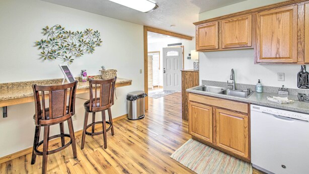 A kitchen with wooden cabinets, a countertop, and a dishwasher. There are two wooden chairs and a trash can.