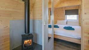 A wooden cabin with a bed, a fireplace, and a door leading to another room. - Creyr Glas Pod -UK41796 (Penybontfawr, near Llanfyllin)