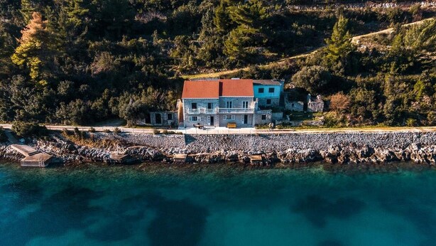 An aerial view of a coastal property with a stone wall and a building with a red roof.