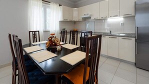 A modern kitchen with white cabinets, a stainless steel refrigerator, and a dining table with wooden chairs.