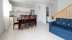 A modern kitchen with white cabinets, a dining table with chairs, and a blue sofa in a living area.