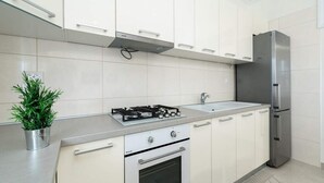 Una cucina moderna con mobili bianchi, un frigorifero in acciaio inox, un fornello a gas e un forno integrato.