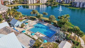 A resort with a large swimming pool surrounded by lounge chairs and umbrellas, a lake, and multiple hotel buildings. - Beach Access Resort Condo with Breath-Taking View (Jupiter)