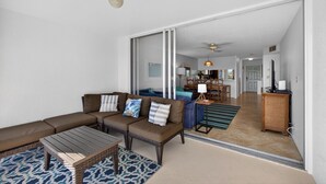 A spacious living area with a sectional sofa, a coffee table, and a patterned rug. A sliding glass door leads to a dining area with a table and chairs. - Beach Access Resort Condo with Breath-Taking View (Jupiter)
