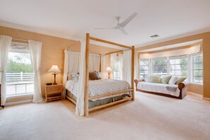 A spacious bedroom with a four-poster bed, a sofa, and large windows offering a view of the outdoors.