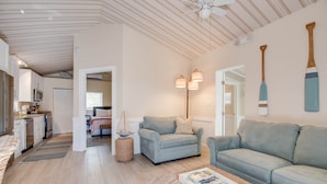Ein modernes Wohnzimmer mit einer Couch, Sesseln und einem Couchtisch. Es gibt eine Küchenzeile mit Schränken und einer Mikrowelle.