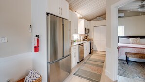 Eine kompakte Küche mit Edelstahlkühlschrank, weißen Schränken, einer Mikrowelle und einem kleinen Spülbecken. An der Wand hängt ein Feuerlöscher und es steht ein Korbkörbchen mit Handtüchern bereit.