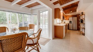 A modern kitchen with wooden beams, a dining area with wicker chairs, and a view of trees through large windows. - 9BR Estate | 3 Homes/2 Pools/Hot tub -30 Min to KW (Monroe County)