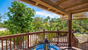 A wooden deck with a glass table and wicker chairs, surrounded by tropical vegetation and a clear sky. - 9BR Estate | 3 Homes/2 Pools/Hot tub -30 Min to KW (Monroe County)