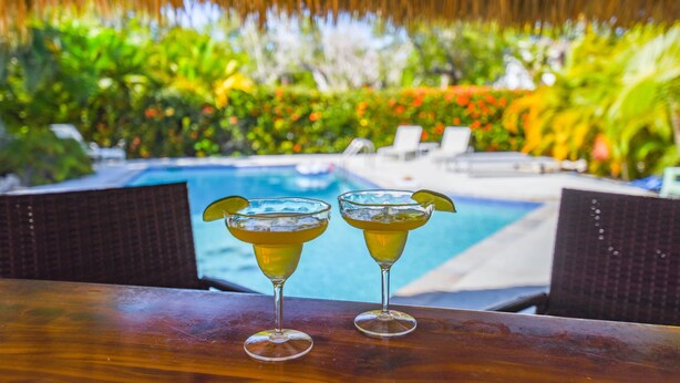 Two cocktails on a wooden table with a pool and lounge chairs in the background. - 9BR Estate | 3 Homes/2 Pools/Hot tub -30 Min to KW (Monroe County)