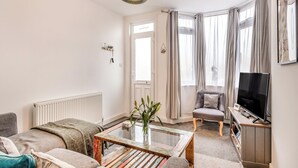 Un salon avec un canapé, une table basse, un téléviseur et une fenêtre avec des rideaux.
