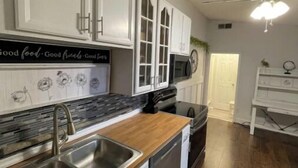 Una cucina con mobili bianchi, un lavello in acciaio inossidabile e un piano di lavoro in legno.