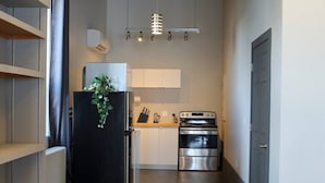 A compact kitchen with a refrigerator, oven, and countertop. - Suite with AC, Industrial Styling (Bedford)
