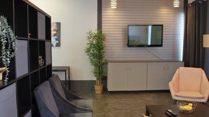 A modern living room with a sofa, a chair, a TV mounted on the wall, and a cabinet. - Suite with AC, Industrial Styling (Bedford)