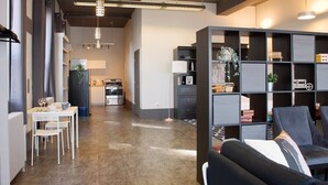 A modern kitchen with stainless steel appliances, a dining area with white furniture, and a black shelving unit with decorative items. - Suite with AC, Industrial Styling (Bedford)