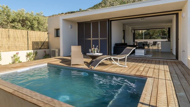Een modern buitenzwembad met een houten terras, ligbedden en een eethoek met tuinmeubilair.