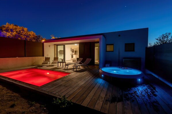Un espace piscine extérieur moderne, doté d’un jacuzzi et de chaises longues.
