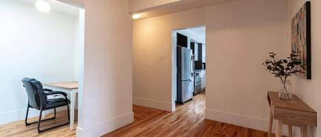 Un apartamento moderno con piso de madera, un comedor con mesa y sillas, una cocina equipada y una pequeña mesita de madera con un jarrón.