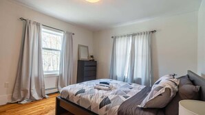 A bedroom with a bed, curtains, a dresser, and a window. - Beautiful & Spacious Apt, AC (Bedford)