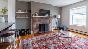 A modern living room with a fireplace, a TV, a bar area, and a large window. - Beautiful & Spacious Apt, AC (Bedford)