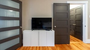 Een kamer met een televisie op een wit kastje, een donkere deur en een hal met een houten vloer.