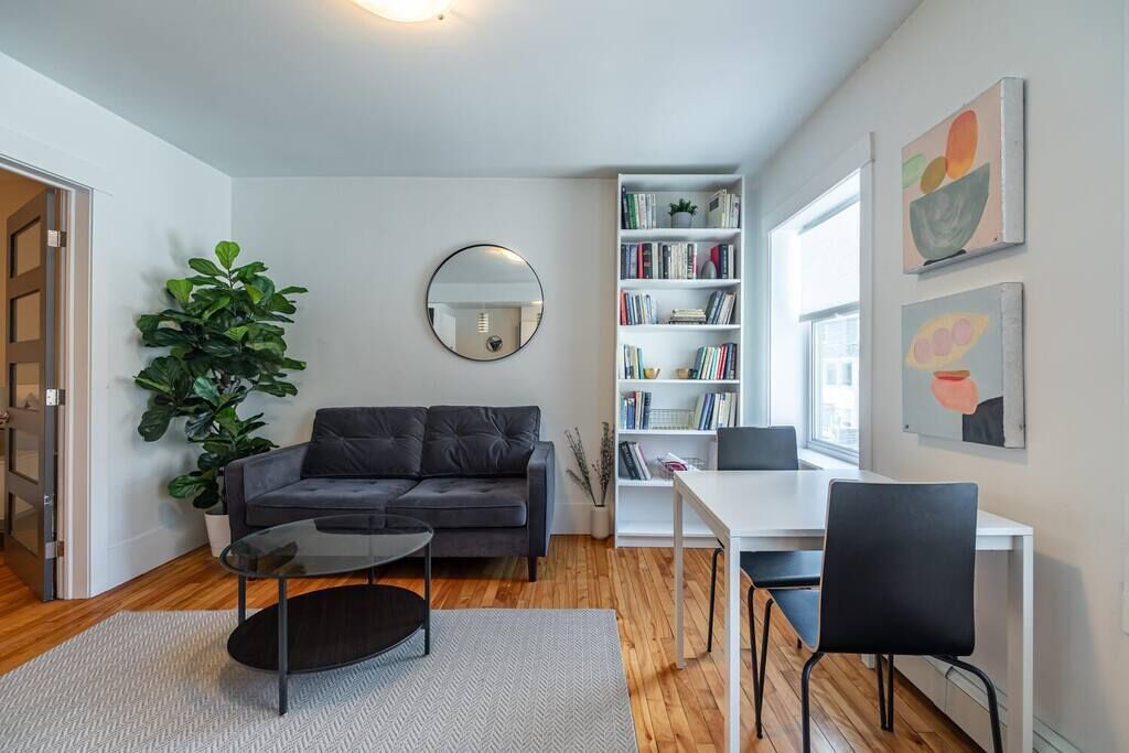 A modern living room with a sofa, coffee table, bookshelf, and a dining area with chairs.