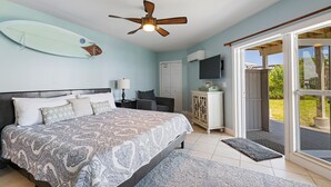 Een slaapkamer met een bed, een plafondventilator, een surfboard aan de muur en uitzicht op het omliggende landschap.