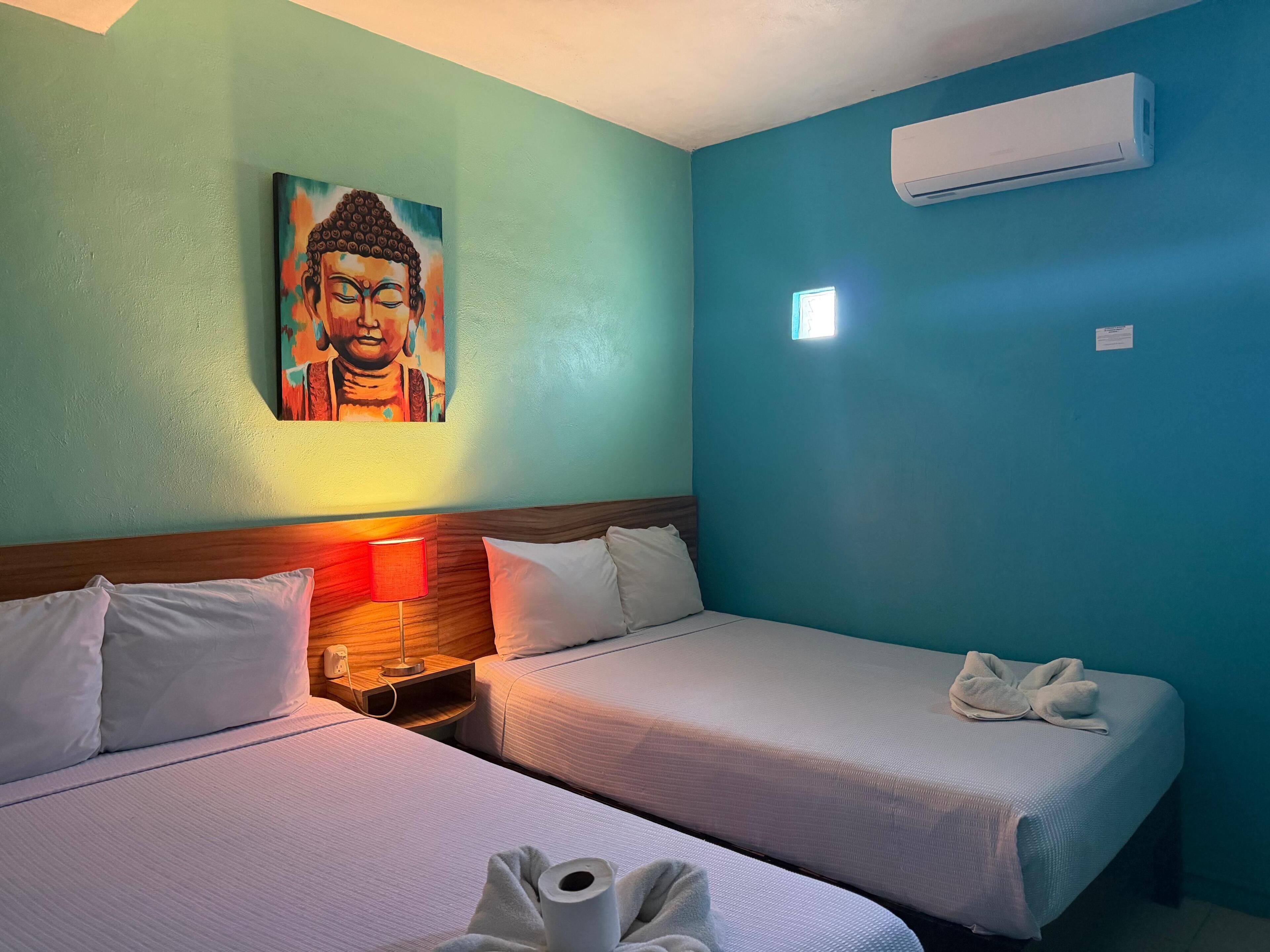 Una habitación de hotel con dos camas, un cuadro en la pared, aire acondicionado y una lámpara de noche.