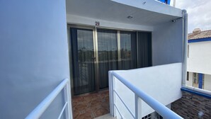 Ein Balkon mit einer Schiebeglastür, weißen Geländern und einem gefliesten Boden.
