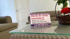 Ein Wohnzimmer mit Glastisch, Rattan-Hocker, einer Couch und einer Tür mit Hinweisschild.