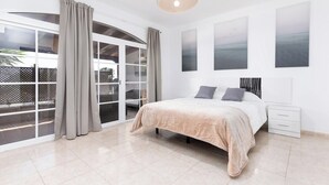 Une chambre moderne avec un grand lit, une table de chevet et une vue sur l’extérieur, accessible par une porte-fenêtre coulissante.