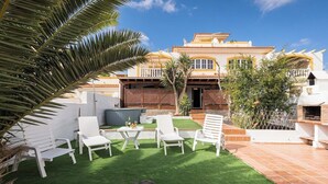 Une terrasse avec des chaises longues blanches et une petite table, un barbecue et une piscine.