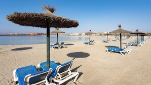 Une plage bordée de rangées de chaises longues et d’ombrelles en chaume.