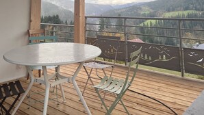 Een houten terras met een tafel en stoelen, met uitzicht op een bergachtig landschap.