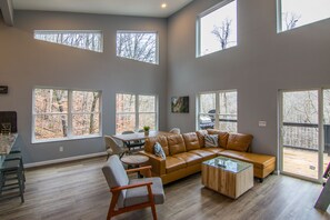 A spacious living room with large windows, a leather sofa, a coffee table, and a dining area.